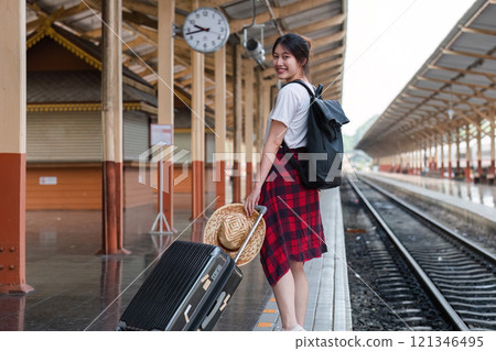 Cute Young Woman Standing at Train Station with Luggage, Ready for Travel Adventure, Smiling and Waiting for Train Arrival Cute Young Woman Standing at Train Station with Luggage, Ready for Travel Adventure, Smiling and Waiting for Train Arrival 121346495