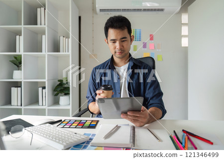 Young Male Graphic Designer Focused on Creative Work at Modern Office Desk with Computer and Design Tools 121346499