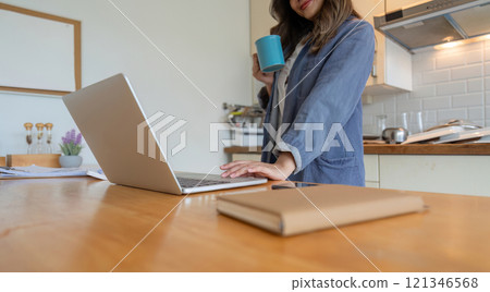Woman Working from Home in Dining Room with Laptop and Coffee Cup in Modern Kitchen Setting Woman Working from Home in Dining Room with Laptop and Coffee Cup in Modern Kitchen Setting 121346568