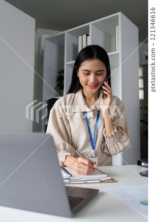 Confident Businesswoman Engaged in a Phone Call at Modern Office Desk with Laptop and Documents 121346616