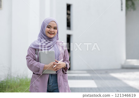 Confident Muslim Girl Student in Hijab Holding Books and Smiling Outdoors, Embracing Education and Modernity in a Bright Urban Setting Confident Muslim Girl Student in Hijab Holding Books and Smiling Outdoors, Embracing Education and Modernity in a Bright Urban Setting 121346619