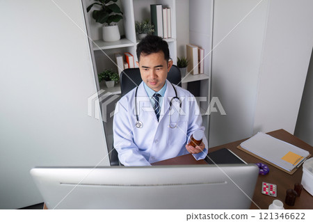 Male Doctor in White Coat Studying Medicine for Healthcare Solutions in Modern Medical Office Environment 121346622