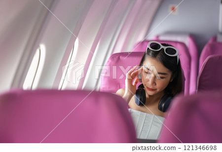 Woman Traveling by Plane, Relaxing in Comfortable Seat with Headphones, Enjoying In-Flight Entertainment, Modern Air Travel Experience 121346698