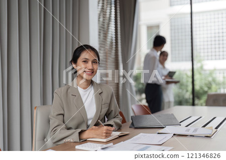 Confident Business Woman in Modern Office Setting with Colleagues in Background 121346826