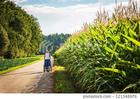 Rear view of disabled handicapped woman in wheelchair and care helper walking on rural path. Rear view of disabled handicapped woman in wheelchair and care helper walking on rural path. 121348978