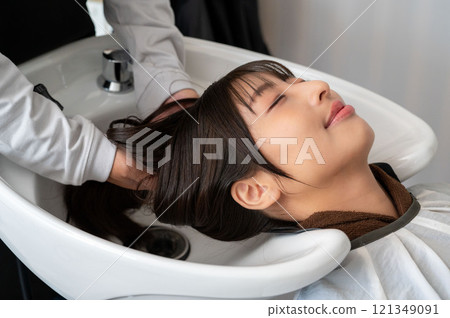 A female customer having her hair washed by a male staff member 121349091