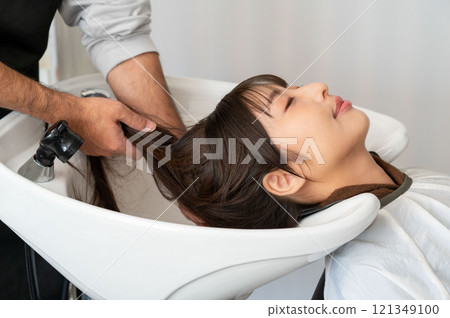 A female customer having her hair washed by a male staff member A female customer having her hair washed by a male staff member 121349100