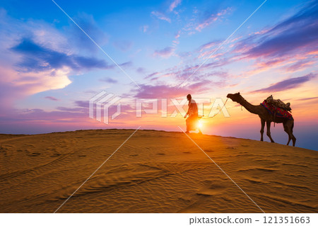 Indian cameleer camel driver camel silhouettes in dunes on sunset. Jaisalmer, Rajasthan, India 121351663