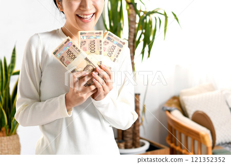 微笑的亞洲年輕女性在室內拿著一疊錢 121352352