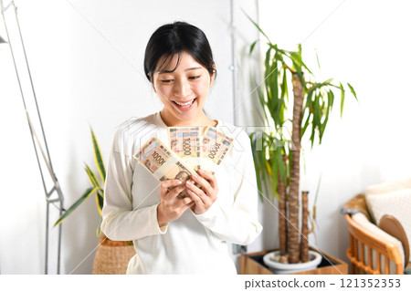 微笑的亞洲年輕女性在室內拿著一疊錢 121352353