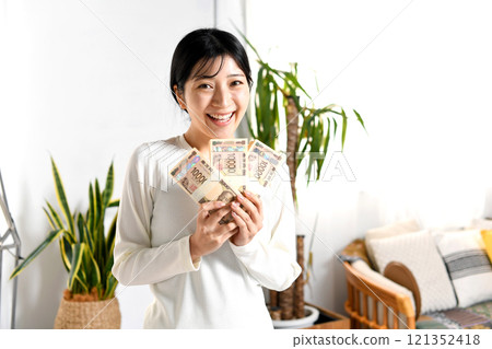微笑的亞洲年輕女性在室內拿著一疊錢 121352418