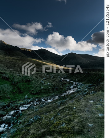 Mountain landscape with a flowing stream under a cloudy sky in early evening light. 121352548