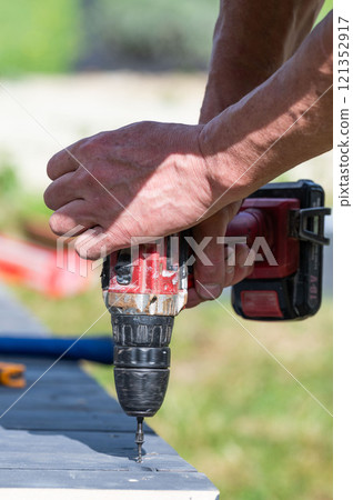 Installation work of a wooden gazebo, the master is screwing screws into the wooden floor. 121352917