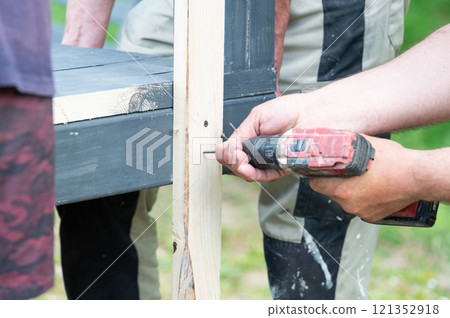 Screwing the board with a screwdriver, installing a wooden gazebo. 121352918