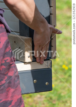 A worker supports the edge of the wall with his hand to compare it with the floor during the installation of a gazebo. A worker supports the edge of the wall with his hand to compare it with the floor during the installation of a gazebo. 121352919
