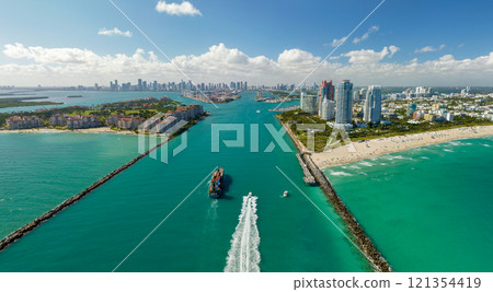 Commercial container ship entering Miami port harbor through main channel near South Beach. Luxurious hotels and residential buildings on waterfront and high skyscraper towers of downtown in distance Commercial container ship entering Miami port harbor through main channel near South Beach. Luxurious hotels and residential buildings on waterfront and high skyscraper towers of downtown in distance 121354419