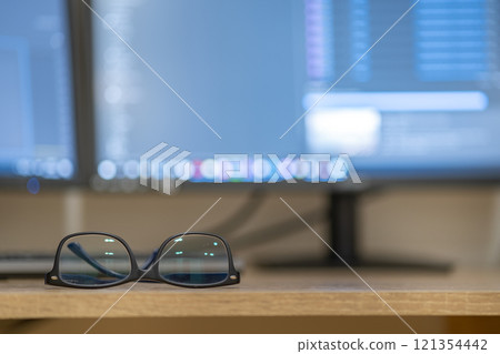 Closeup of protective glasses on an empty desk with blurred computer screen on background. 121354442