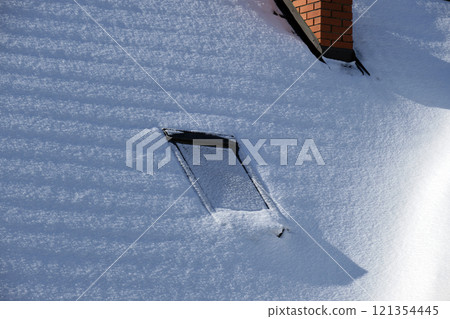 Closeup of house roof top with attic windows covered with snow in cold winter. Tiled covering of building in wintertime weather Closeup of house roof top with attic windows covered with snow in cold winter. Tiled covering of building in wintertime weather 121354445