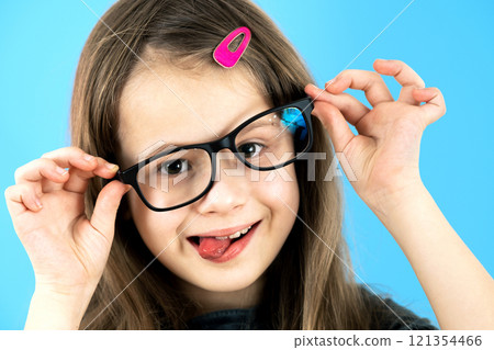 Close up portrait of a funny child school girl wearing looking glasses isolated on blue background. 121354466