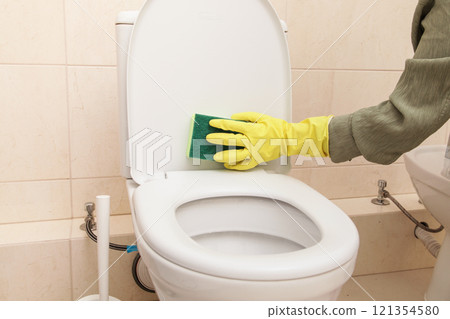 Home Cleaning in Protective Yellow Gloves, Green sponge. Cleans Toilet Home Cleaning in Protective Yellow Gloves, Green sponge. Cleans Toilet 121354580