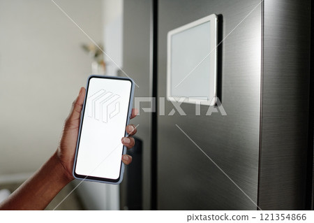 Unrecognizable female hand demonstrating smartphone with white screen near refrigerator Unrecognizable female hand demonstrating smartphone with white screen near refrigerator 121354866