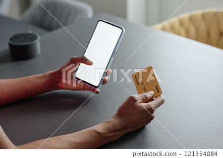 High angle shot of unrecognizable female hands holding smartphone with total white screen and golden credit card High angle shot of unrecognizable female hands holding smartphone with total white screen and golden credit card 121354884