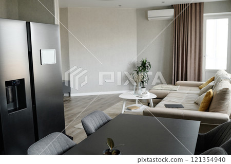 Modern dining area with graphite fridge and same colored table, light living room with comfortable couch and multicolored cushions 121354940