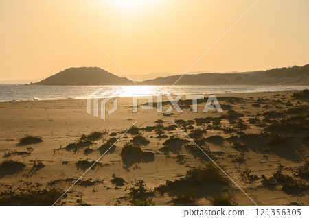 Golden sunset over a tranquil beach with gentle waves and distant hills in the background. Golden sunset over a tranquil beach with gentle waves and distant hills in the background. 121356305