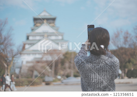 一位女性旅客用智慧型手機拍攝大阪城的後視圖 一位女性旅客用智慧型手機拍攝大阪城的後視圖 121356651