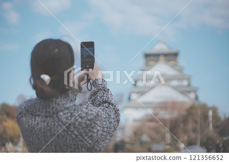 一位女性旅客用智慧型手機拍攝大阪城的後視圖 121356652