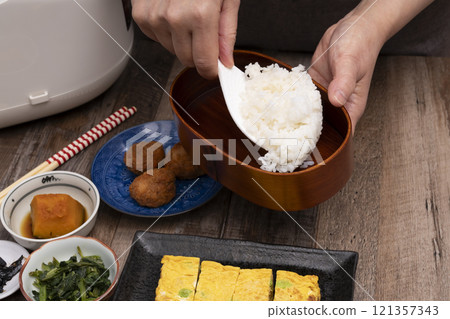 Packing rice and side dishes into a lunch box Packing rice and side dishes into a lunch box 121357343