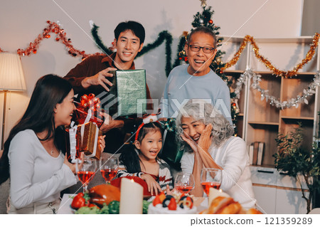 Portrait of Asian family exchanging presents during christmas at home. Attractive happy people holding gift box, celebrate holiday thanksgiving, xmas eve tradition in living room in house together. 121359289