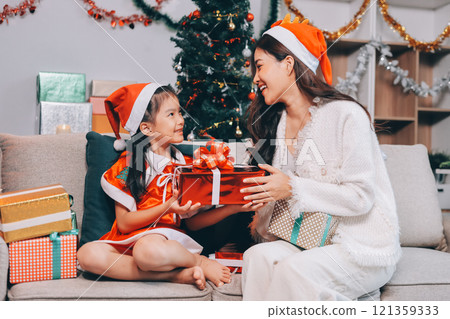 Merry Christmas and Happy Holidays. Cheerful mom and her cute daughter girl exchanging gifts. Parent and little child having fun near tree indoors. Merry Christmas and Happy Holidays. Cheerful mom and her cute daughter girl exchanging gifts. Parent and little child having fun near tree indoors. 121359333