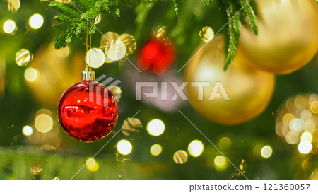 A close-up of a red ornament hanging on a Christmas tree, surrounded by golden decorations and glowing festive lights. The soft bokeh effect creates a warm, magical holiday atmosphere. A close-up of a red ornament hanging on a Christmas tree, surrounded by golden decorations and glowing festive lights. The soft bokeh effect creates a warm, magical holiday atmosphere. 121360057