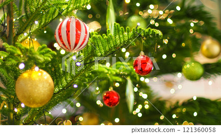 A festive Christmas tree adorned with red, gold, and striped ornaments, illuminated by soft white fairy lights. The vibrant colors and bokeh effect create a cheerful holiday ambiance. 121360058