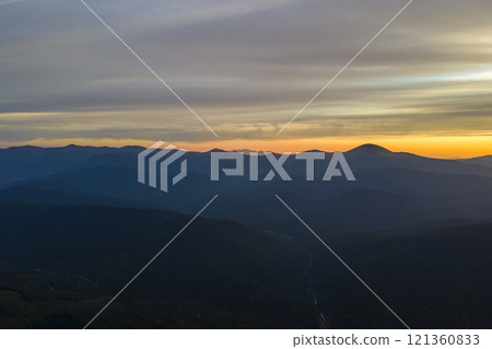 Aerial view of dark mountain hills with bright sunrays of setting sun at sunset. Hazy peaks and misty valleys in evening Aerial view of dark mountain hills with bright sunrays of setting sun at sunset. Hazy peaks and misty valleys in evening 121360833