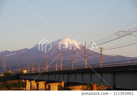 A revival livery 381 series express train, Yakumo, runs across a bridge over the Hino River toward the snow-capped foot of Mt. Oyama. 121363061