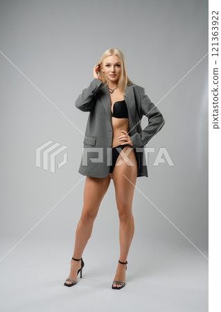 A model poses confidently in a blazer and swimwear on a neutral backdrop 121363922