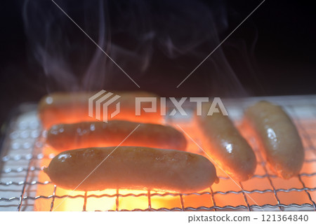 Grilling wieners on a charcoal grill with rising smoke 121364840