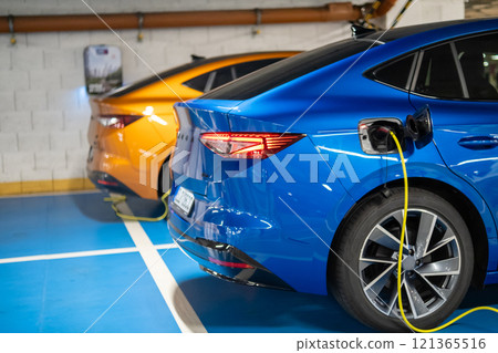 Two electric cars are charging in a sleek parking garage with bright colors and innovative layout 121365516