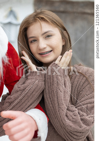 Portrait of young caucasian beautiful woman blond hair smiling in sweater with snow on Christmas Day. with braces. Happy girl in good mood smile showing teeth looking at camera. Portrait of young caucasian beautiful woman blond hair smiling in sweater with snow on Christmas Day. with braces. Happy girl in good mood smile showing teeth looking at camera. 121365560