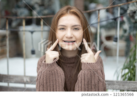 Portrait of young caucasian beautiful woman blond hair smiling in sweater with snow on Christmas Day. with braces. Happy girl in good mood smile showing teeth looking at camera 121365566