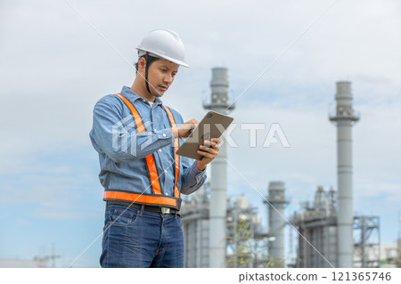 Man engineer with tablet working factory producing electricity oil energy. Construction manager oil refinery in petrochemical. improvement inspector Industrial worker working power plant. 121365746