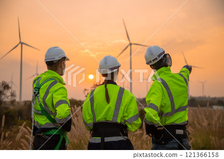 Back view, Team engineer wearing safety uniform discussed plan about renewable energy at station energy power wind in evening when sunset. Technology environment reduce global warming problems. 121366158