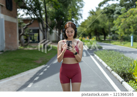 Young beautiful woman sportswear workout clothes using smartphone and listening to music with headphones standing relax in park during exercise the morning. fitness healthy concept. 121366165