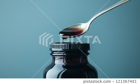 Close-Up of Clear Cough Syrup Bottle with Spoon Dropping Liquid Against a Blue Background 121367481