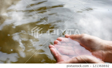 一個男人在熱氣騰騰的露天柏木浴池裡洗澡，用手舀起熱水的場景。 121368692