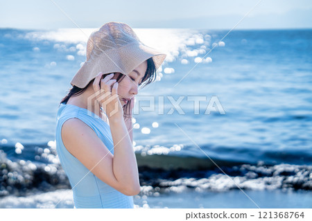 A woman in a straw hat refreshing herself at the beach 121368764