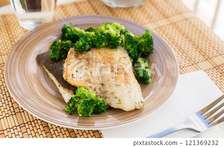 Fried fillet of sea bass with garnish of broccoli on black warm stone plate 121369232