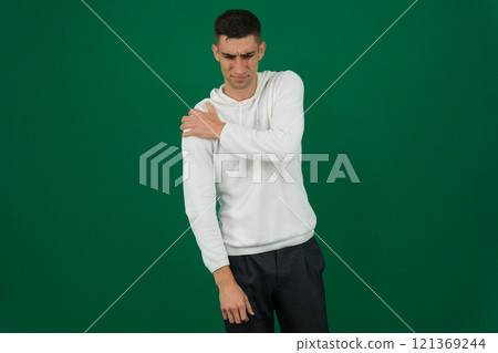 Young asian man experiencing shoulder pain in his bedroom, showing discomfort with a grimace. 121369244